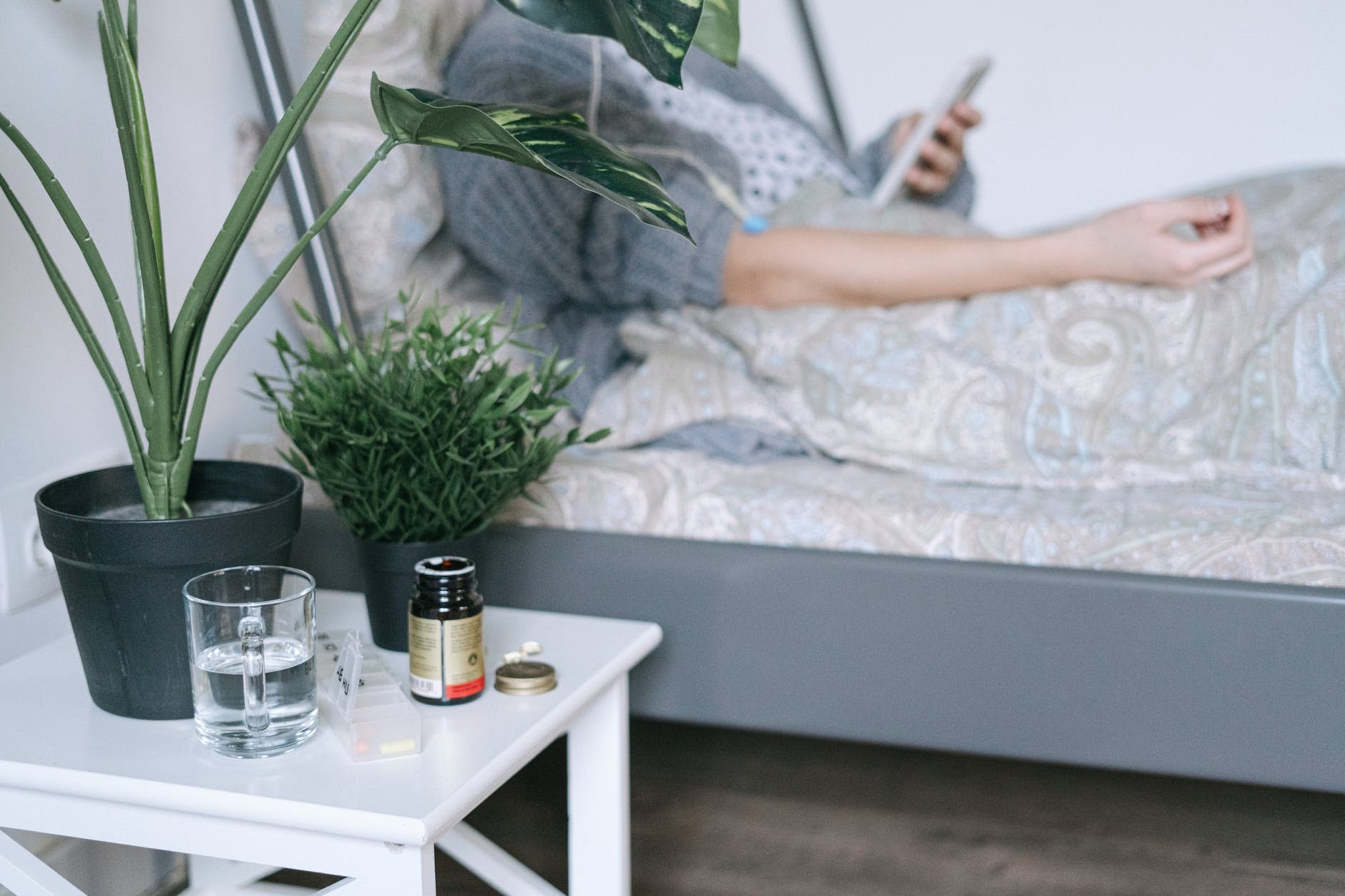 a person sitting in bed with medicine and a glass of water next to them