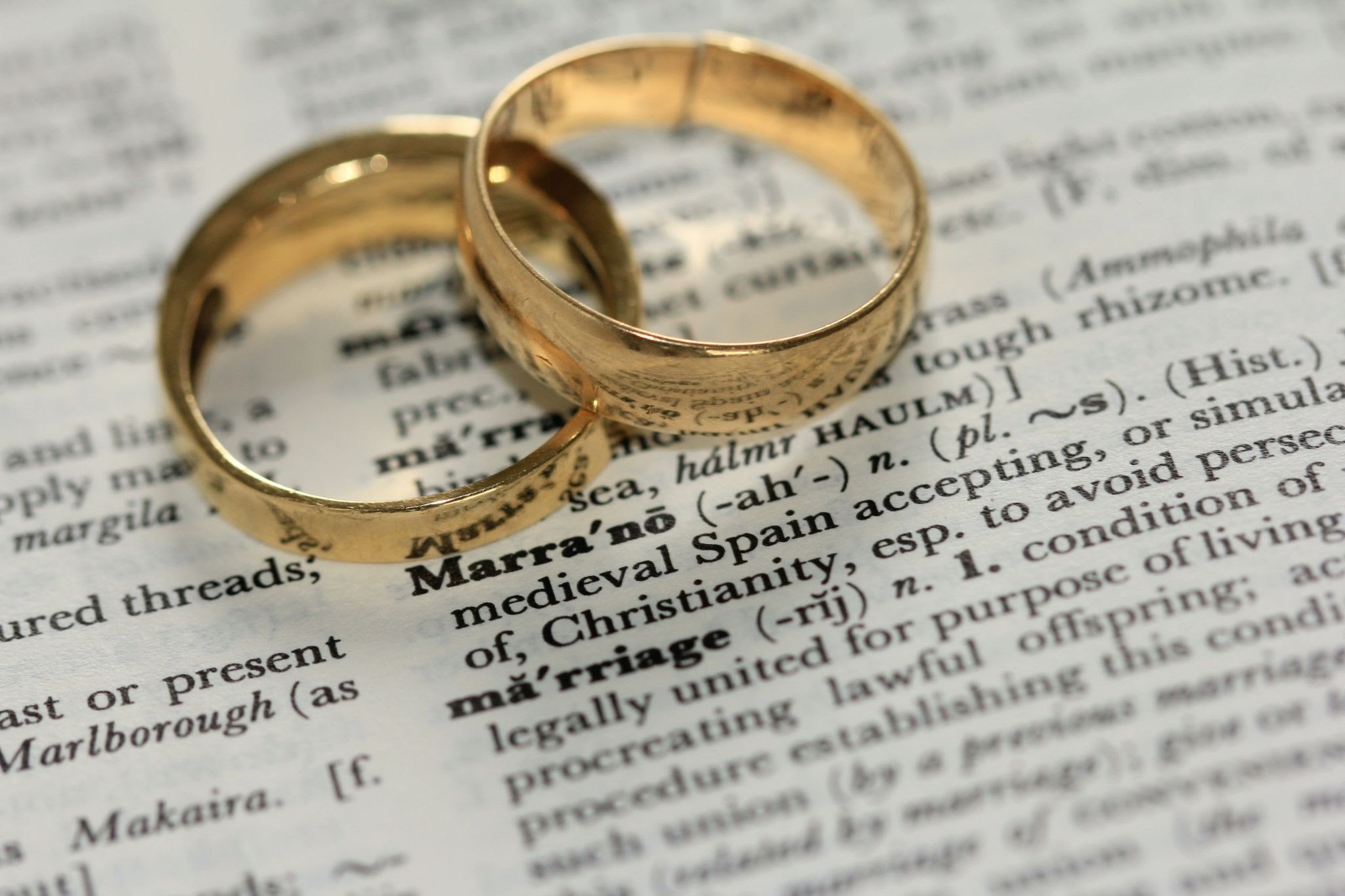 Wedding rings atop a dictionary open to the marriage definition