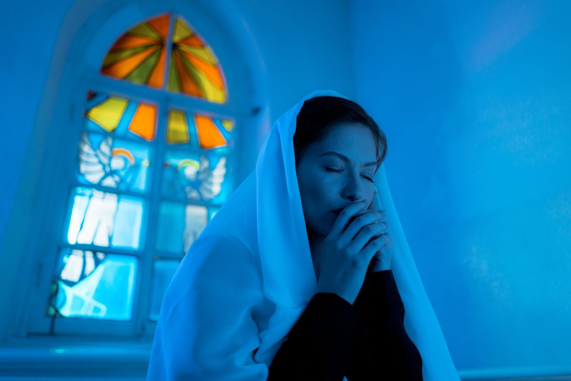 Woman in veil praying in dimly lit church.