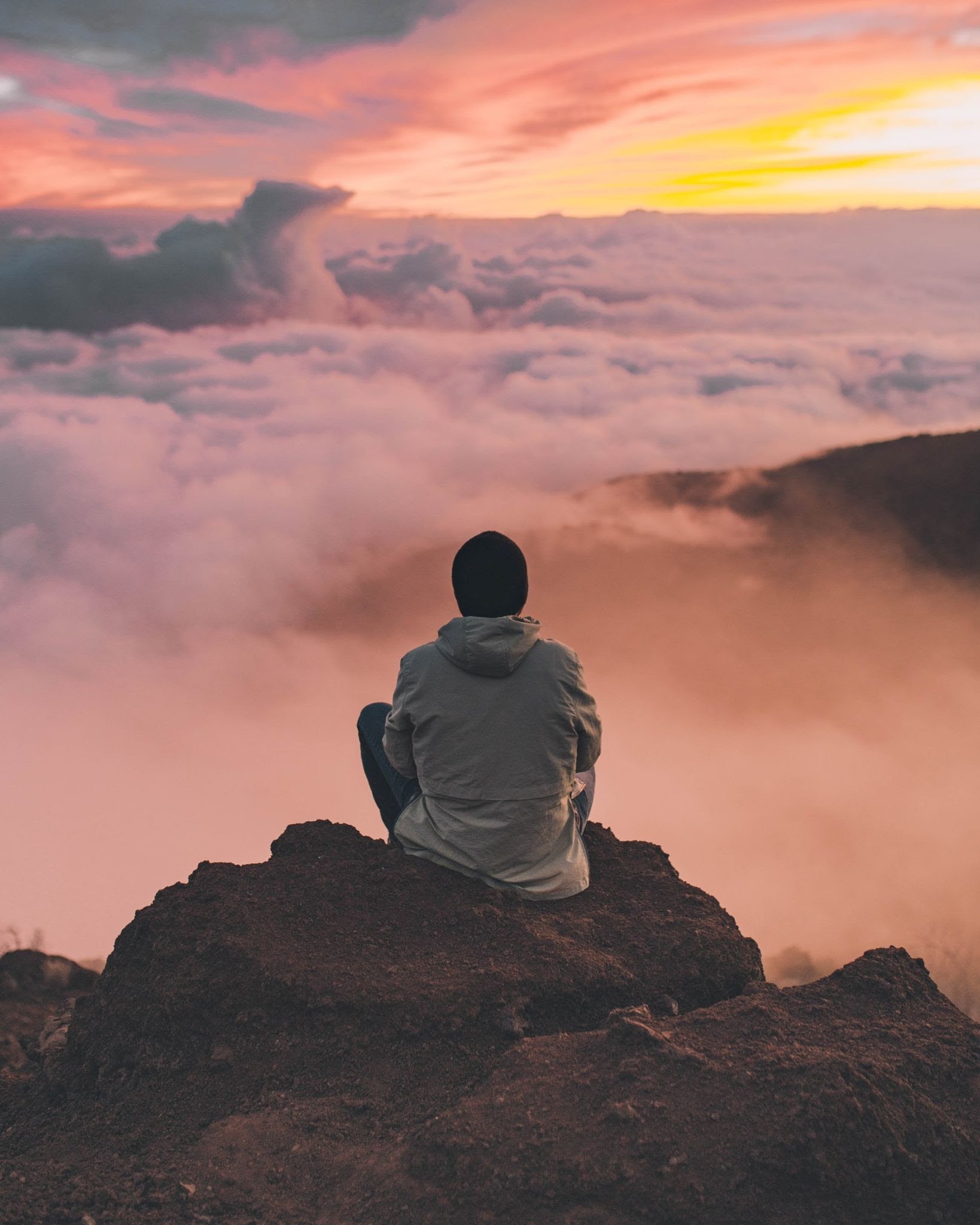 a person sitting on a rock and looking out at the clouds