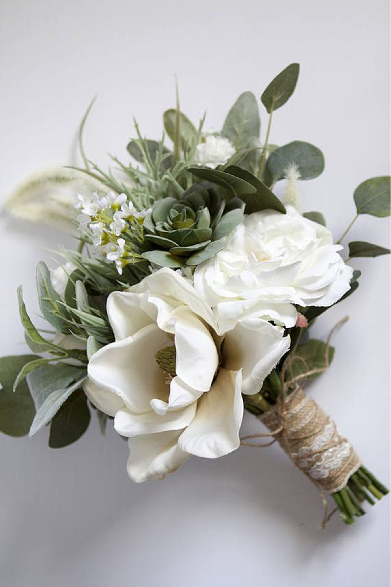 A bouquet of white roses and eucalyptus leaves wrapped in rustic twine and ribbon.