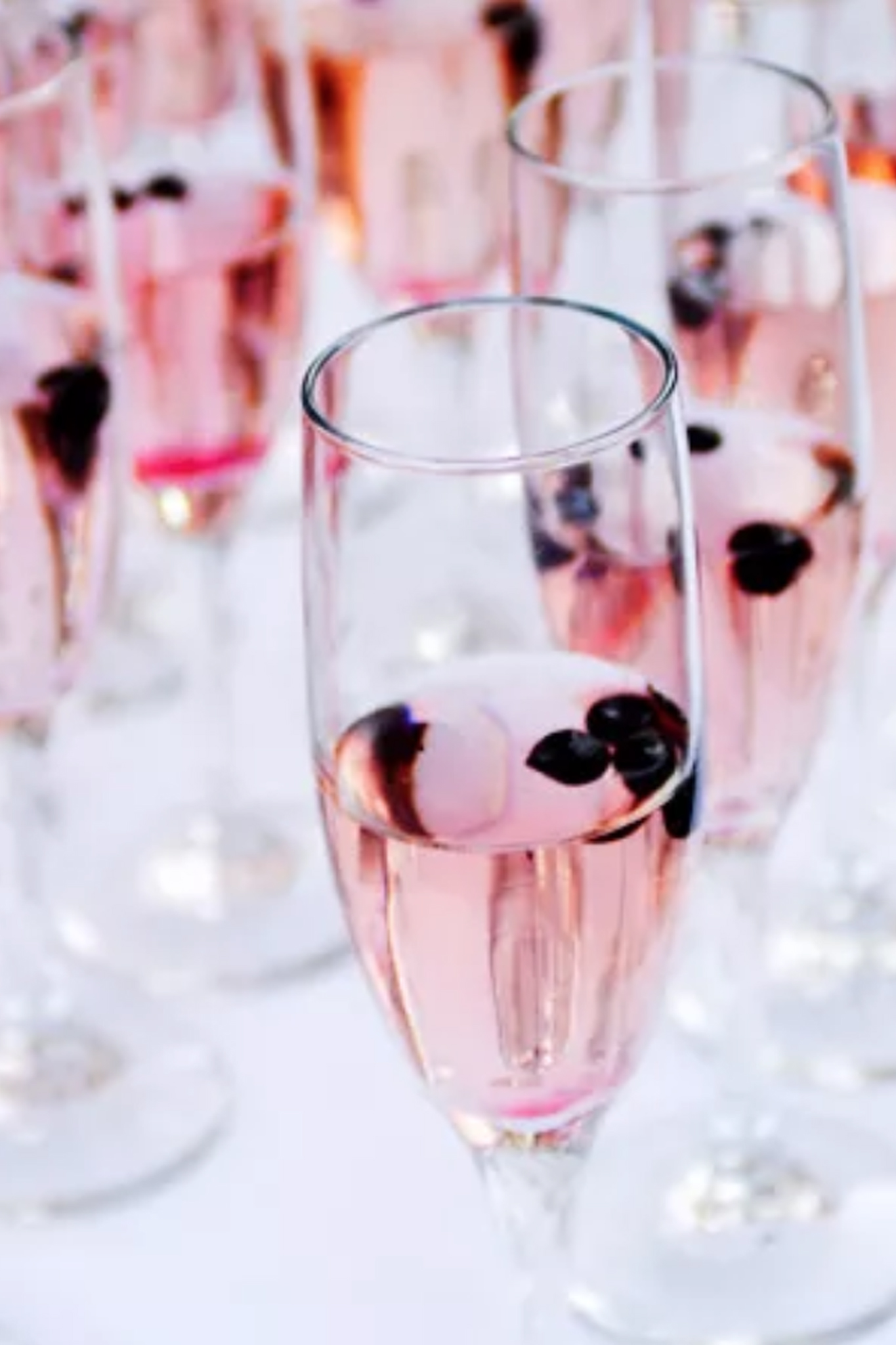 Champagne glasses in a row filled with pink champagne and berries.