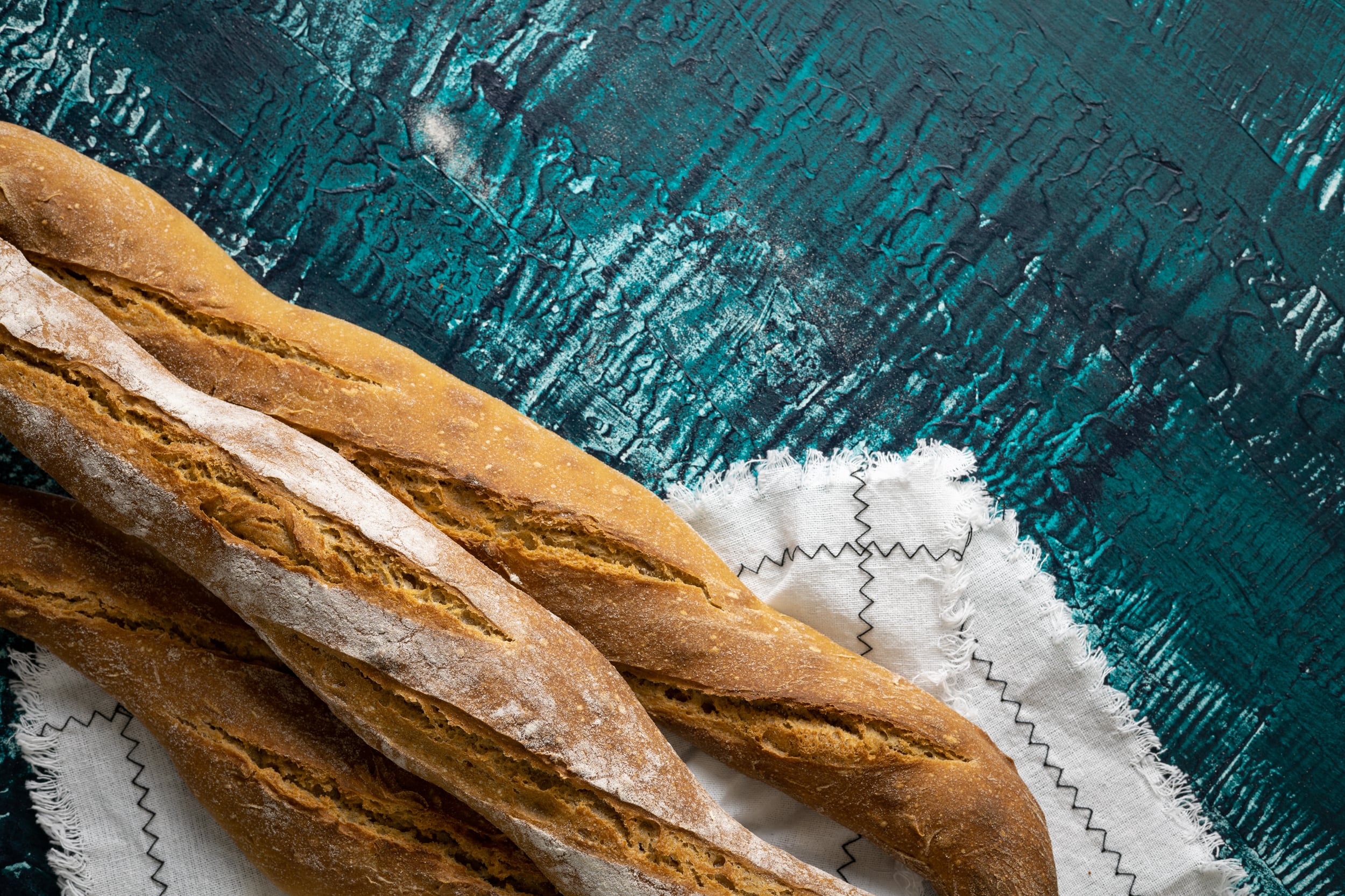 A few baguettes and a white cloth on a blue-green background