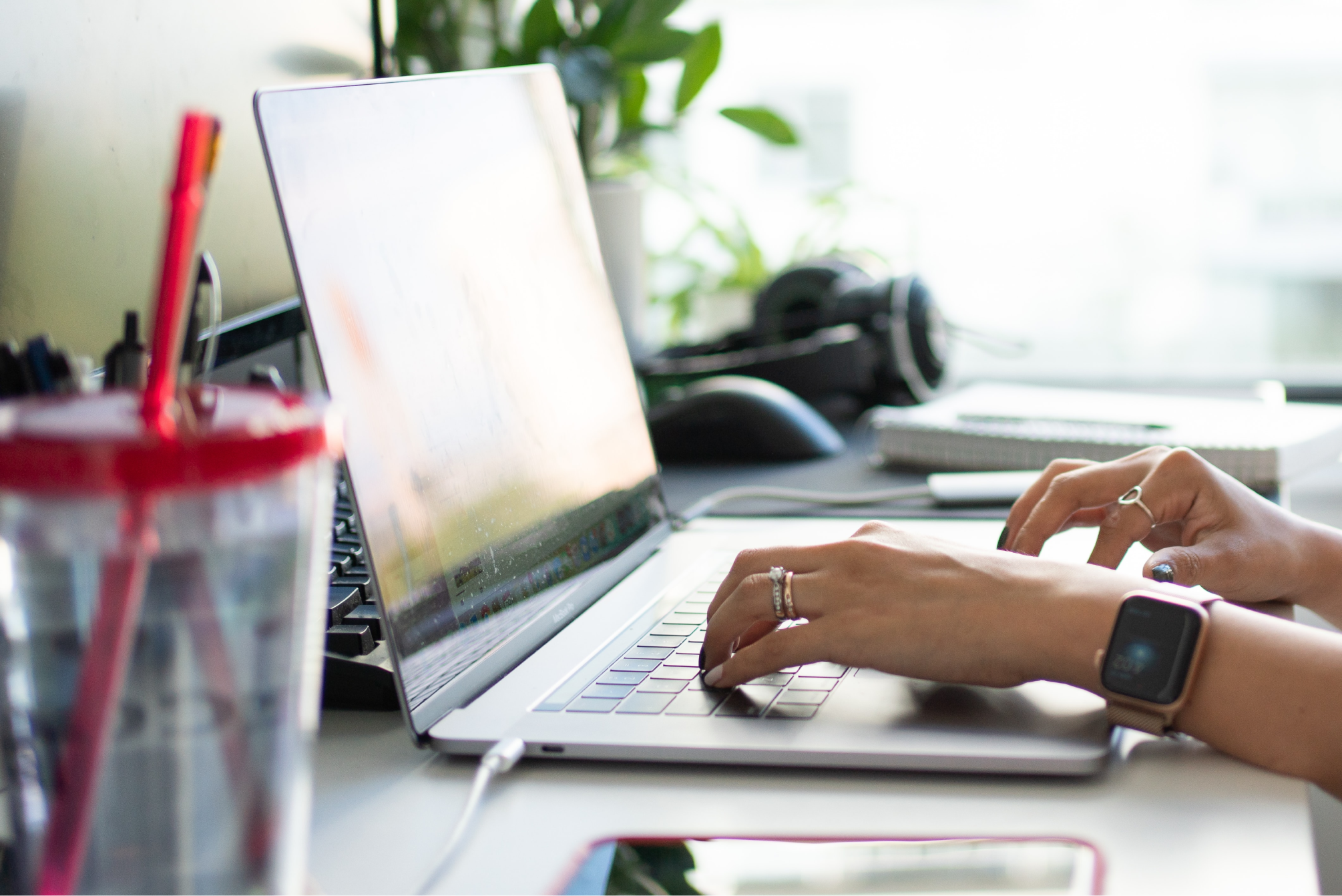Laptop with person typing with her cup and phone on the table beside her