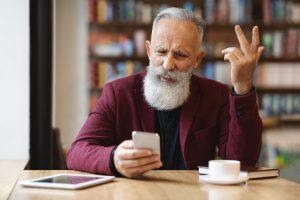 An eldery man annoyed while using a phone.