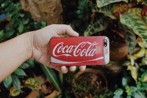 A girl holding a phone wtih a Coca-cola logo.