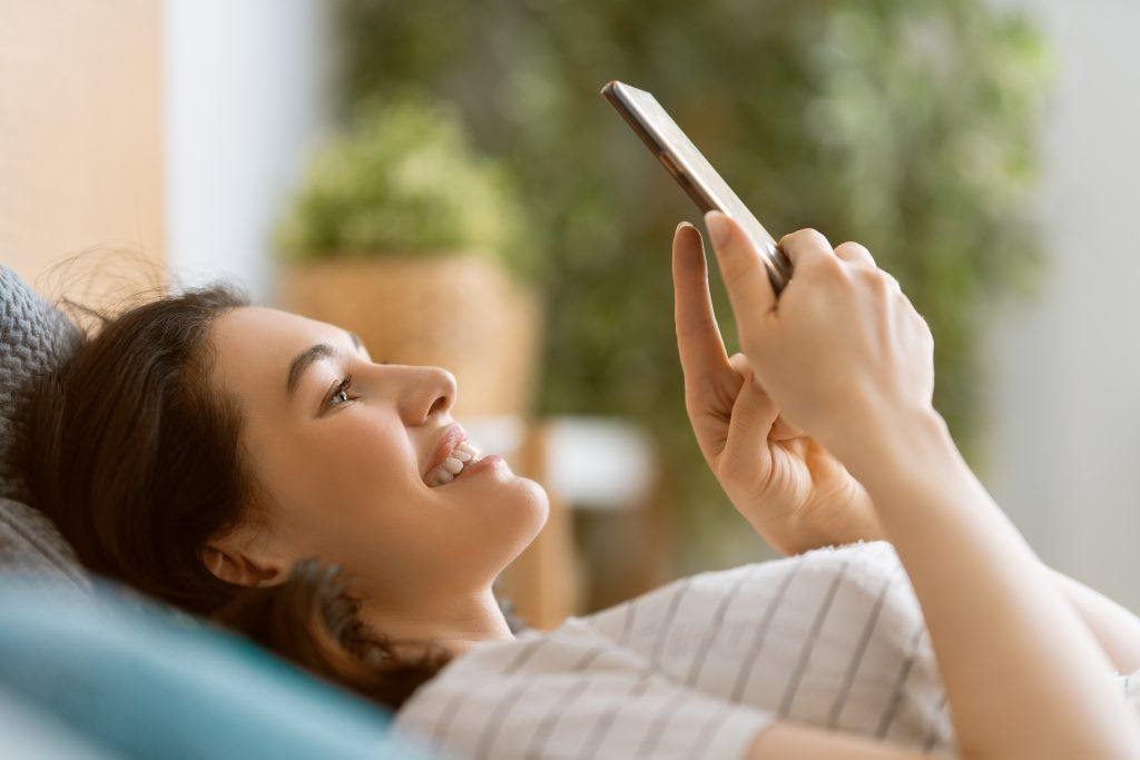 A woman smiling while looking at story content on her phone, showing the value of storytelling and why it is essential for modern marketing.