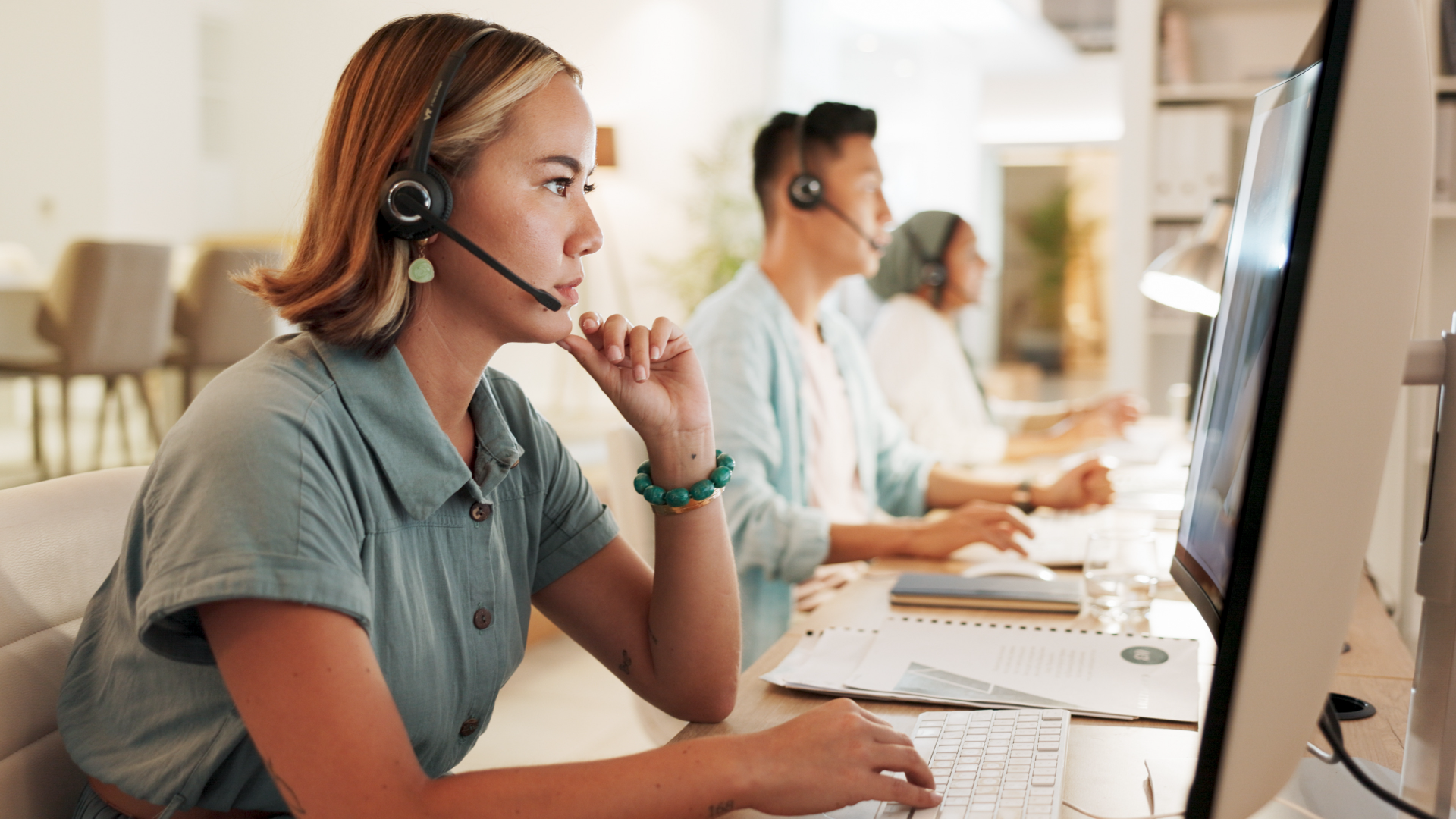 Contact center agents at work - a female agent is looking at the computer screen while wearing a headset. 