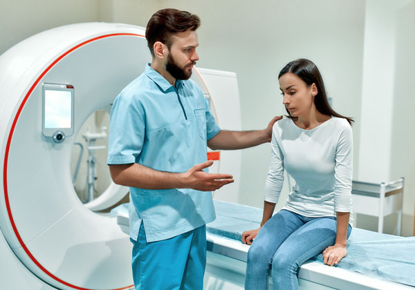 Male nurse is explaining something to a female patient, the patient is sitting on the bed of a MRI machine.