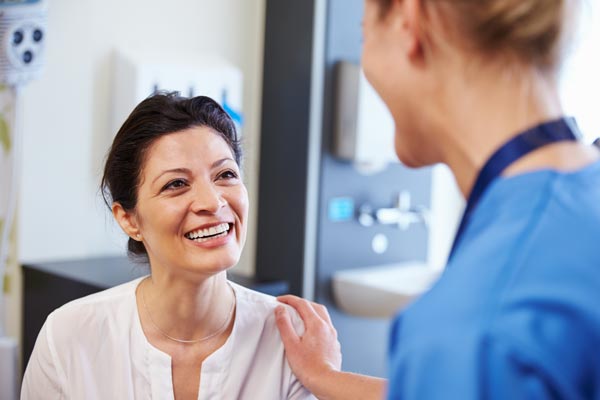 Nurse is comforting female patient, both are smiling.