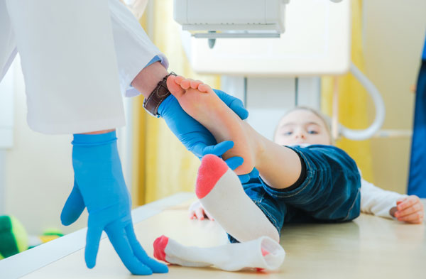 A Doctor holding young girl's foot, girl is lying on the x-ray table.