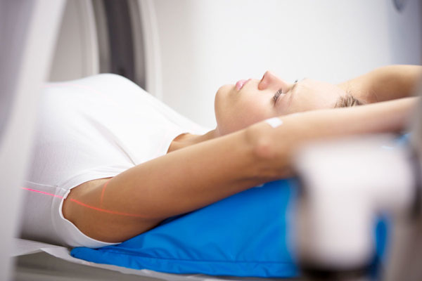 Young woman lying in the Resonance machine with her arms over head.