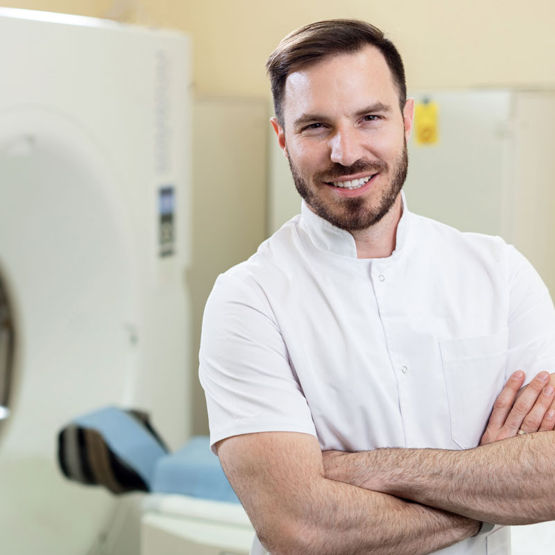 A smiling man standing in front of magnetic resonance machine.