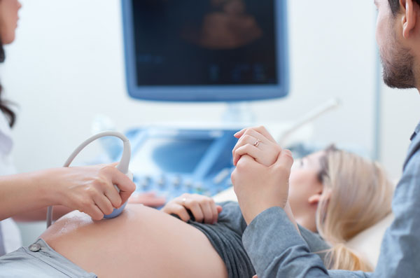 Pregnant woman on the USG examination, her partner is holding her hand.