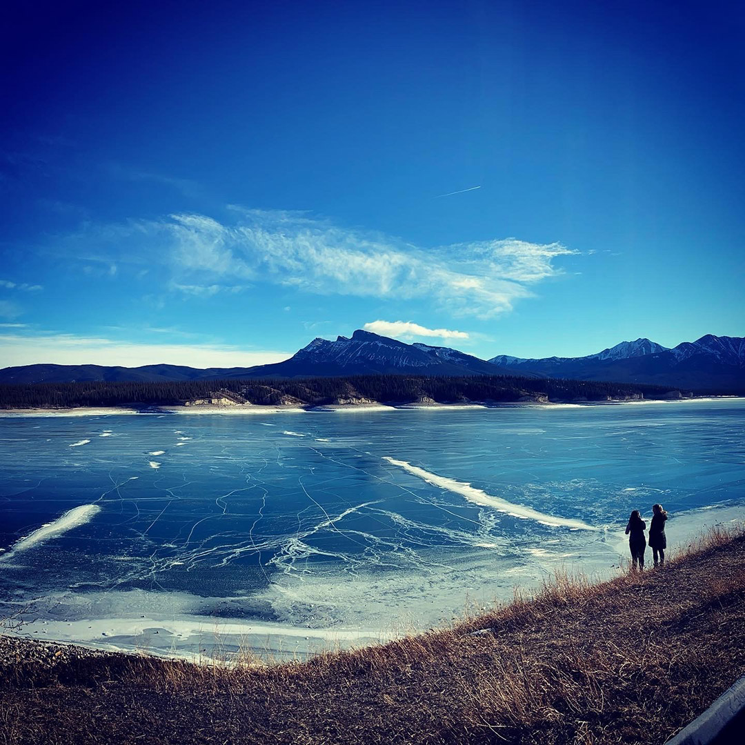 Looking across a frozen Abraham Lake towards the mountains against the bright blue sky