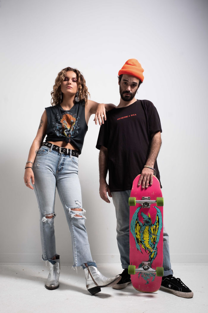 Artist Grey Zeigler standing next to another collaborator in front of a white background with grunge inspired outfits.