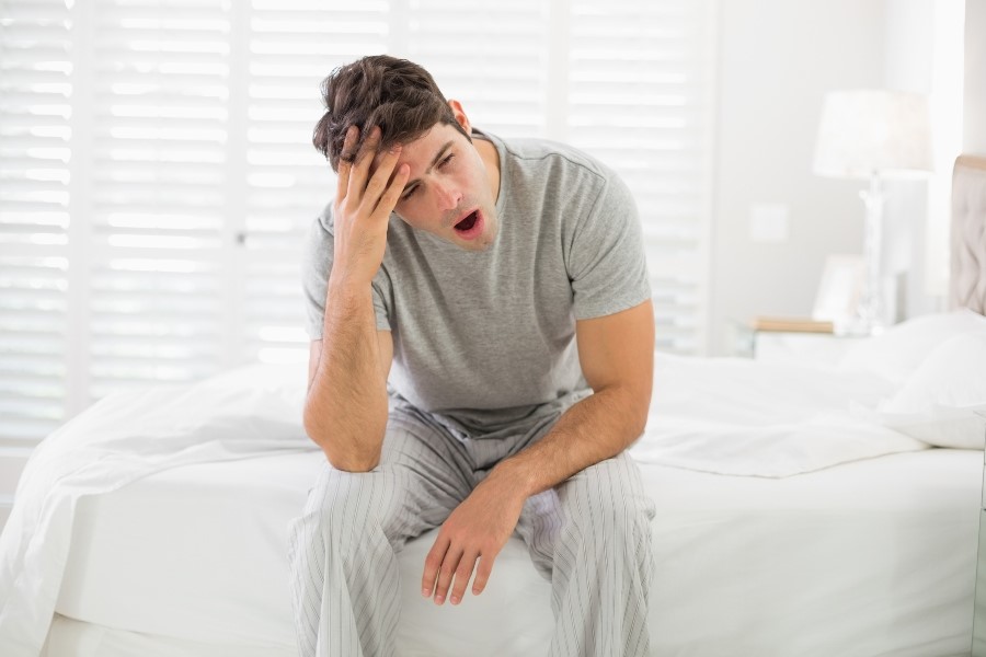 Man yawning while sitting on bed