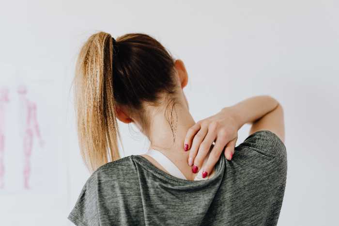 A woman with a ponytail wearing grey rubbing the back of her neck