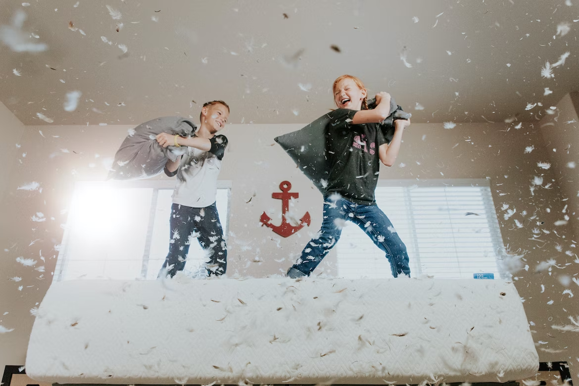 Two young boys having a pillow fight on a bed with feathers flying everywhere