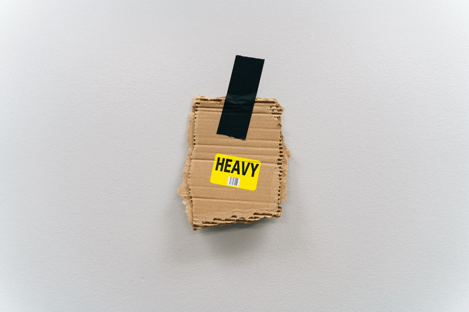 A piece of cardboard taped to a wall with black tape and a yellow sticker that says "Heavy" on it