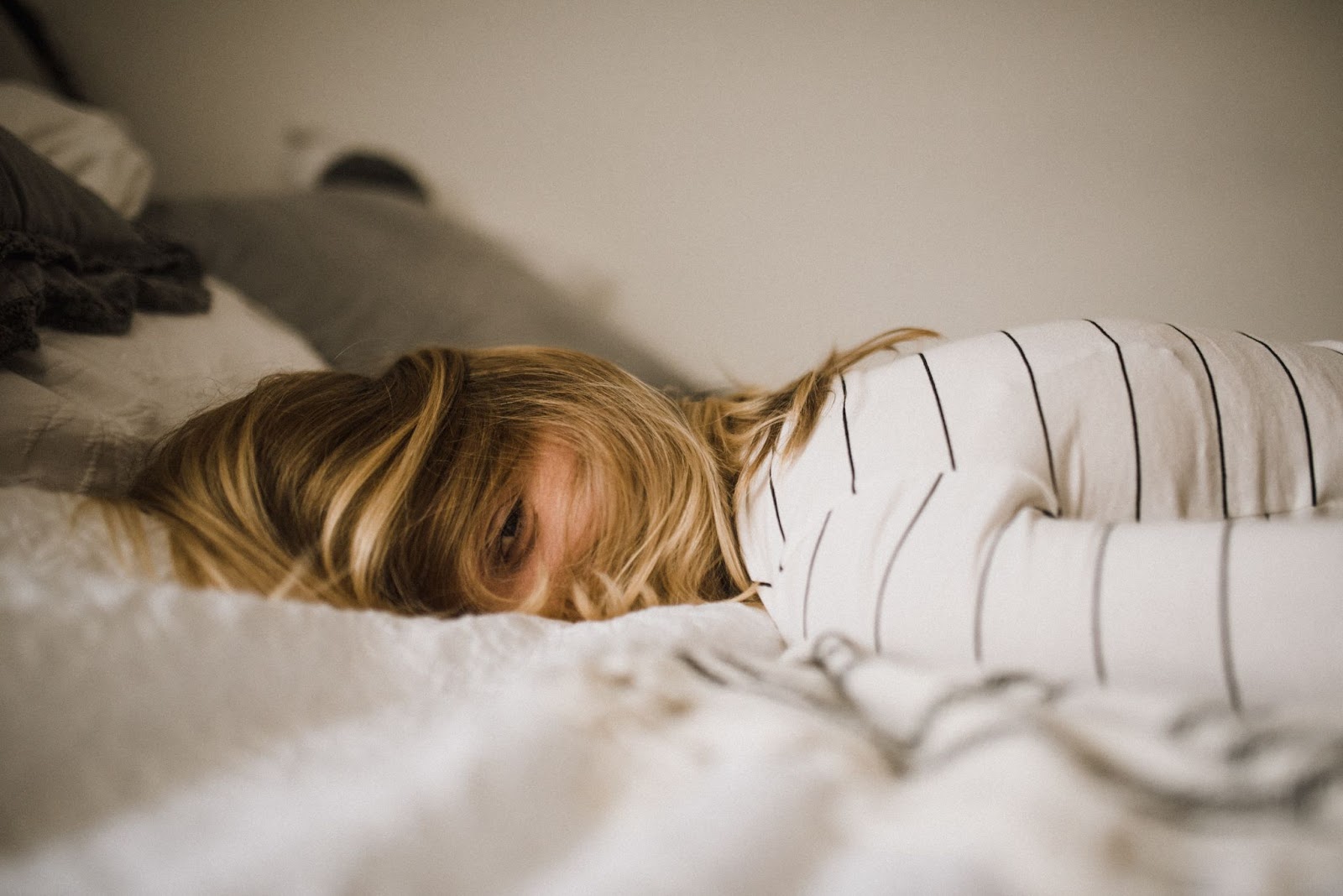 A young blonde girl wearing a white shirt with stripes lying on her stomach on a bed