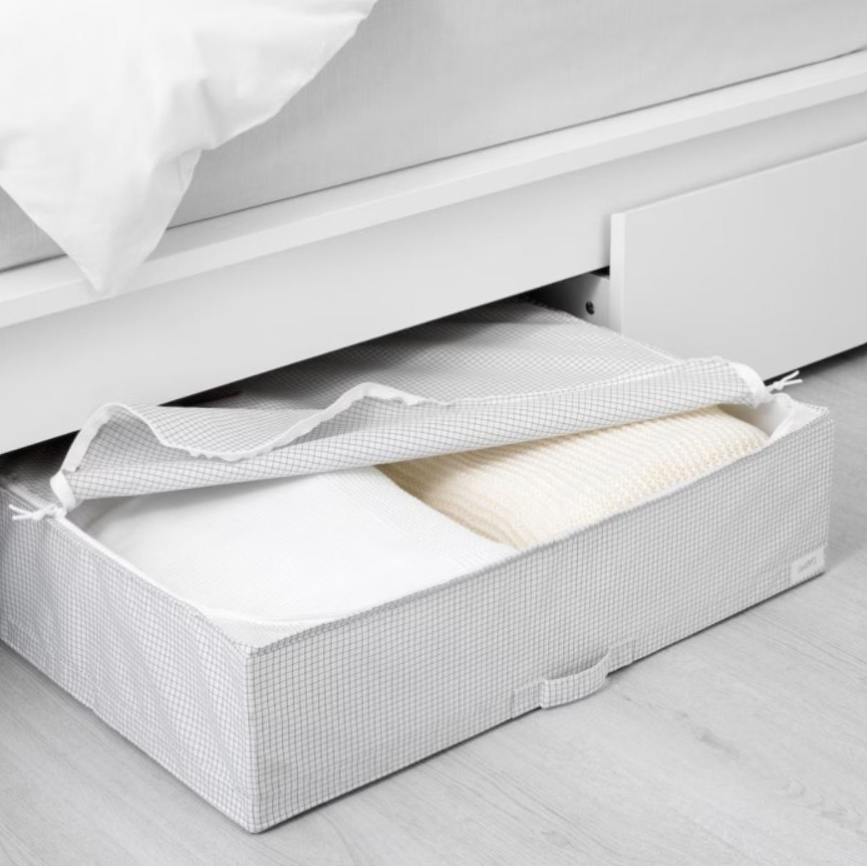 A white checkered STUK Storage Case coming out from under a bed frame with the lid partially open