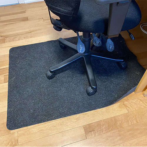 An office chair on a mat sitting on a hardwood floor