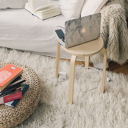 A white fuzzy rug in a living room with a small wooden table and a MacBook sitting on it
