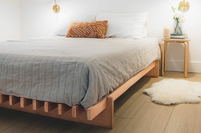The No Fuss Plus bed frame with a mattress and bedding on a wooden floor with white walls next to a nightstand