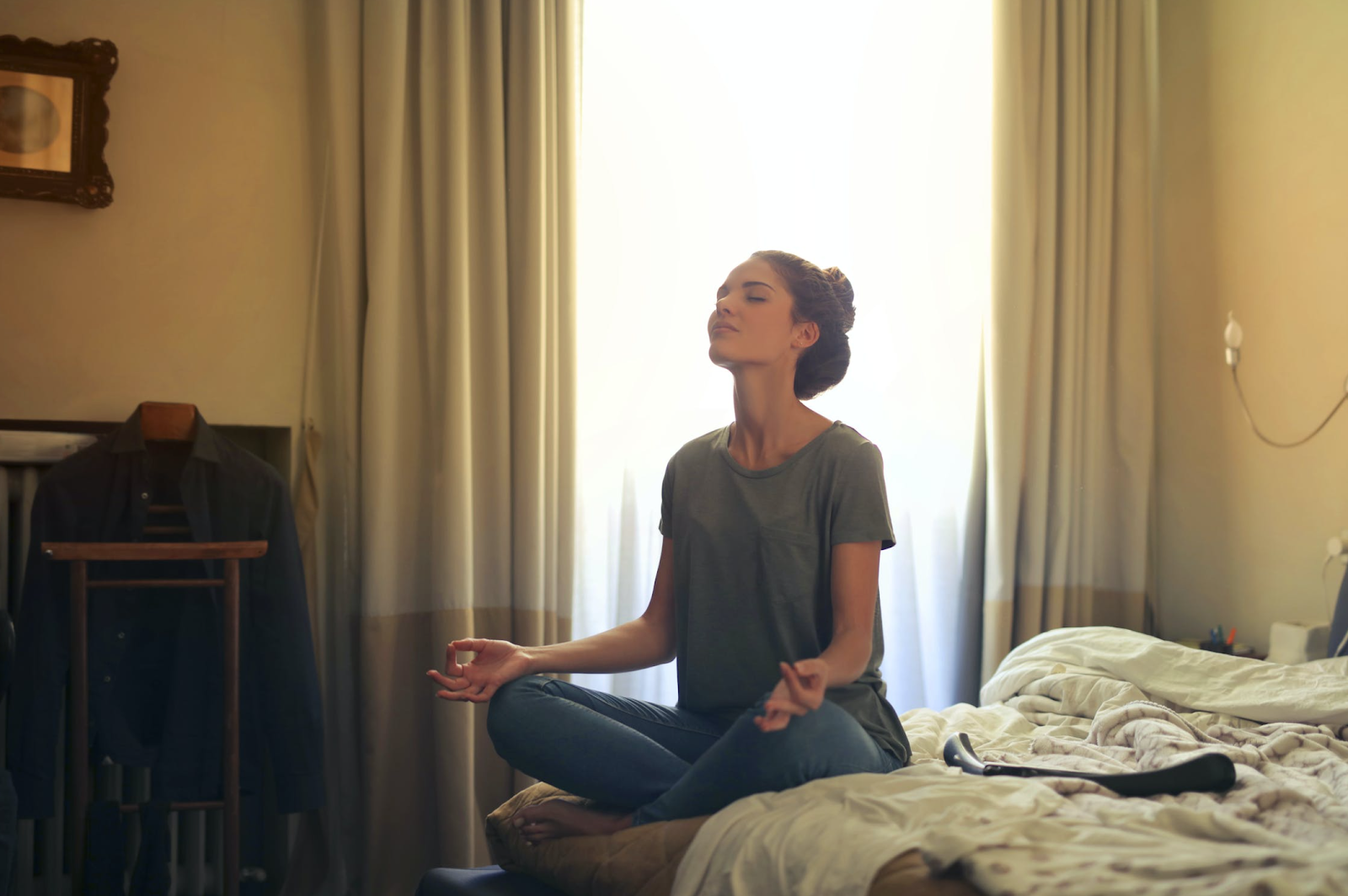 A woman with crossed legs sitting on her bed and meditating.