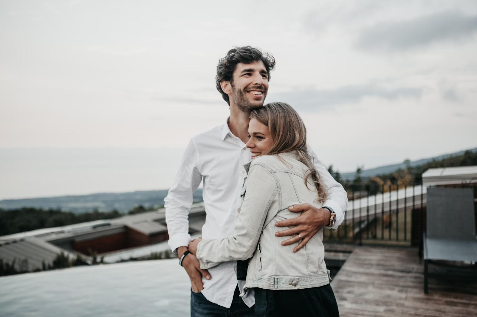 Man and woman hugging on a porch outside.