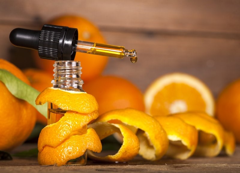A bottle of orange oil surrounded by oranges and orange peels.