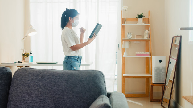 Asian business woman wearing mask using tablet working call video conference with customer in living room from home when social distancing stay at home and self quarantine time, coronavirus concept. Free Photo