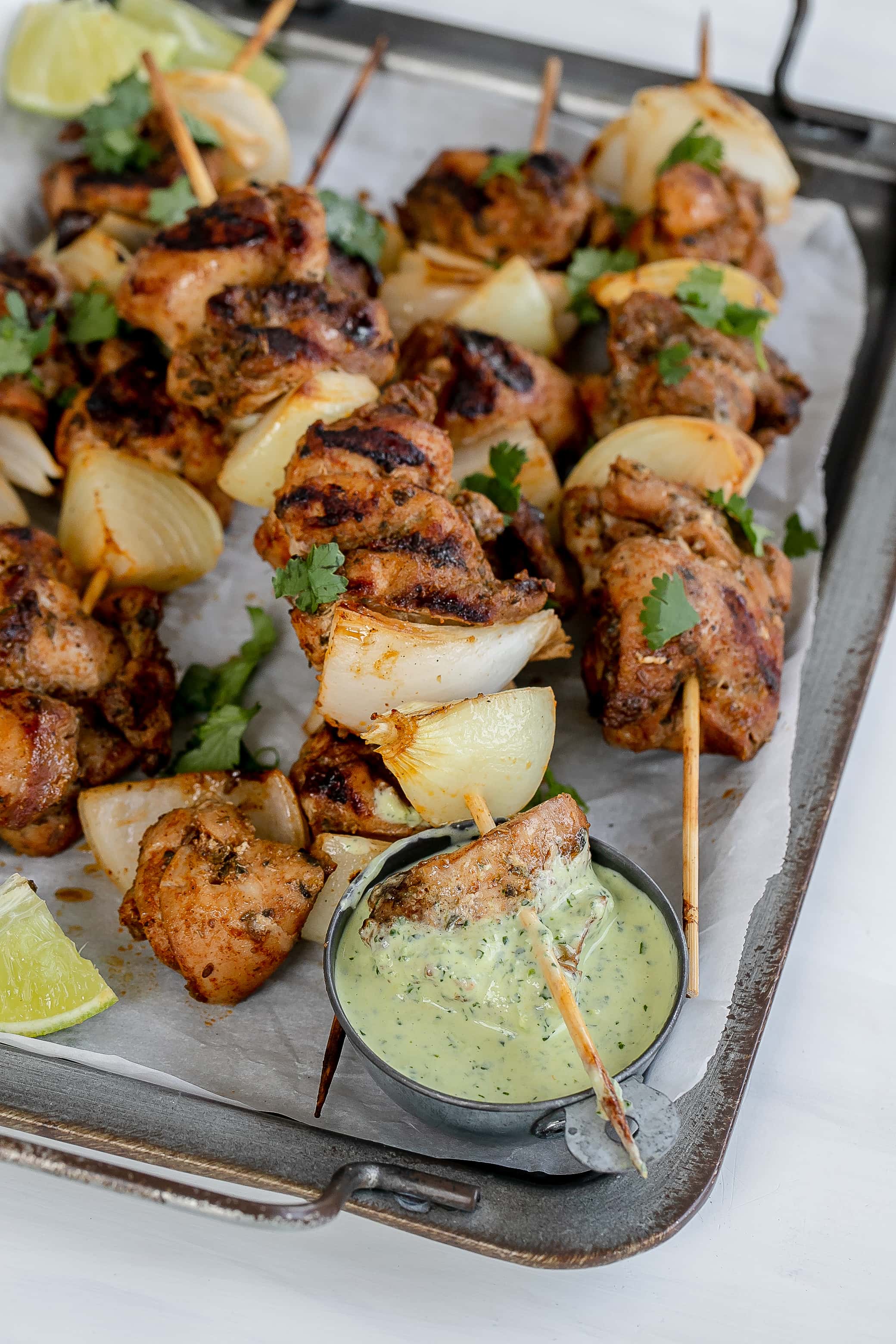 Peruvian chicken skewers and aji verde sauce on baking sheet.
