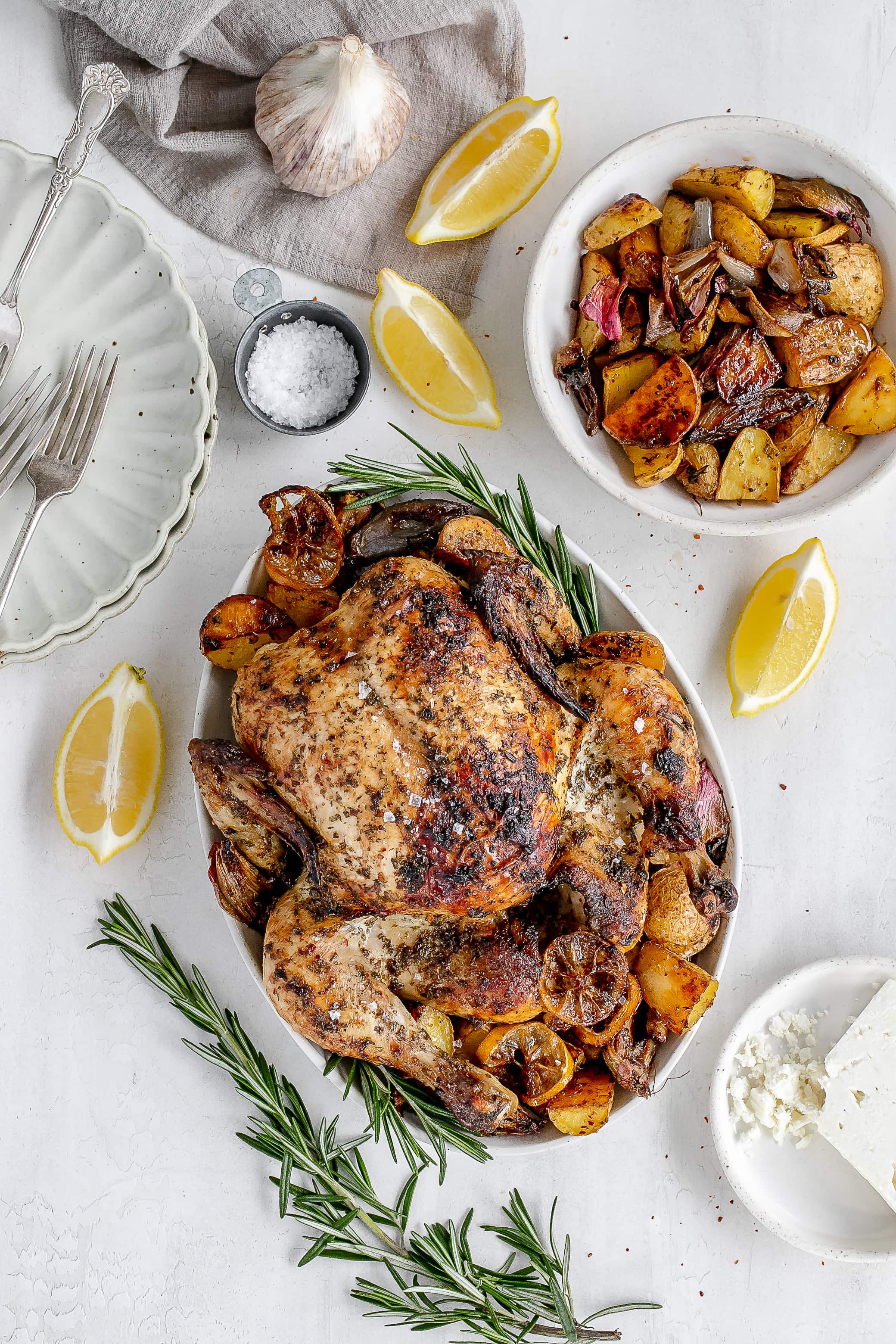 Whole Greek roast chicken on a platter with potatoes.