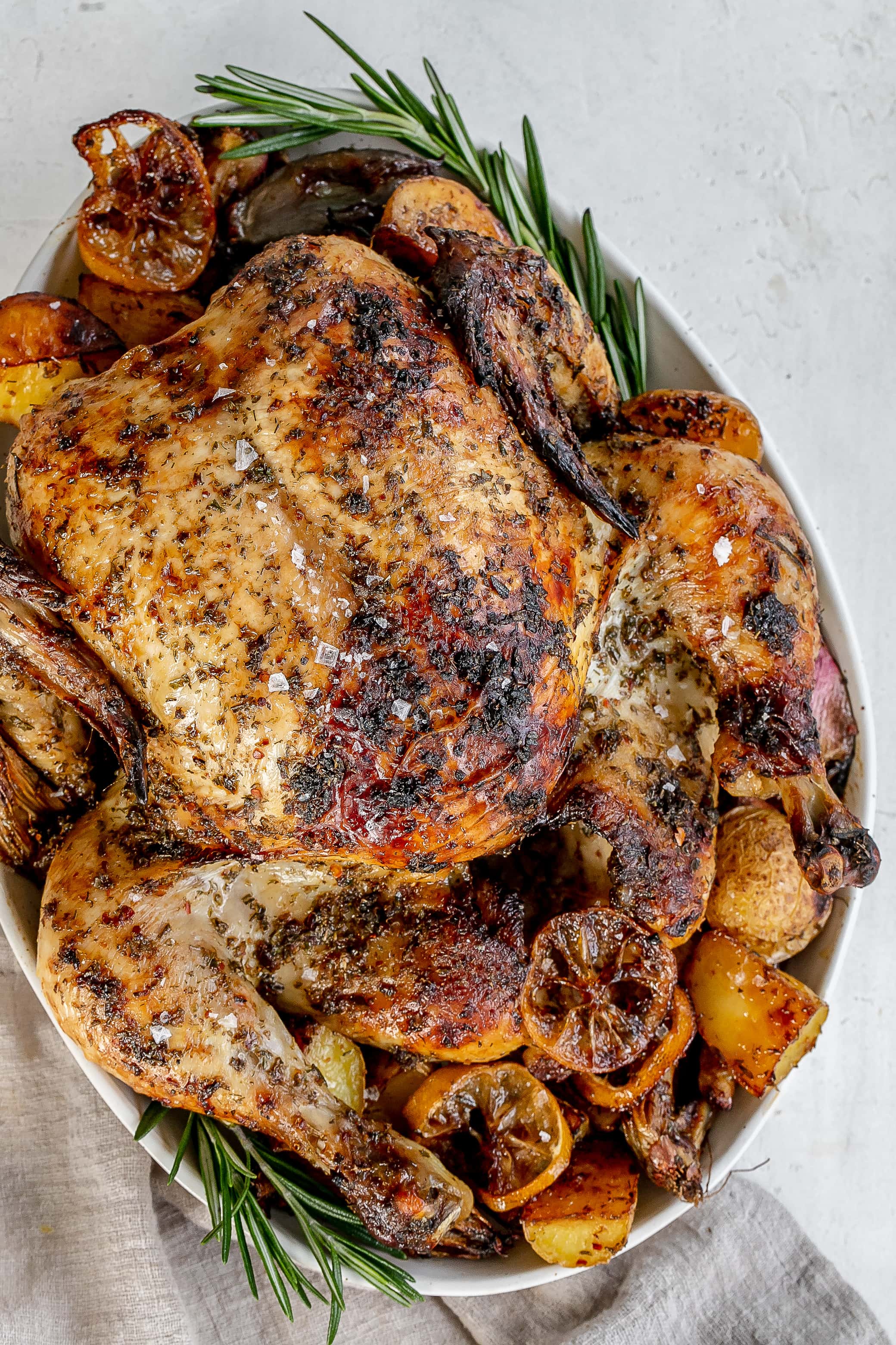 Whole Greek roast chicken on a platter with potatoes.