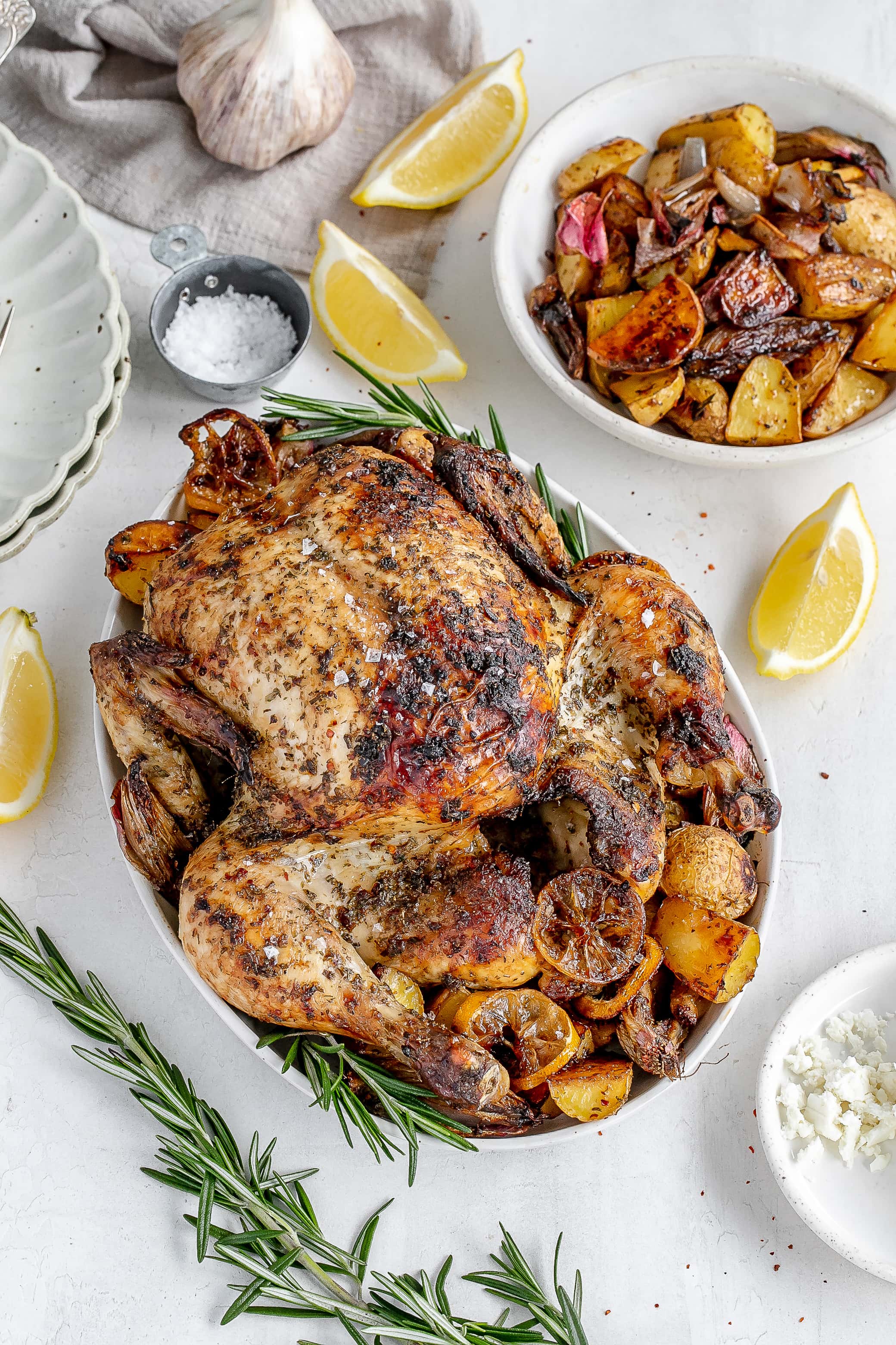 Whole Greek roast chicken on a platter with potatoes.