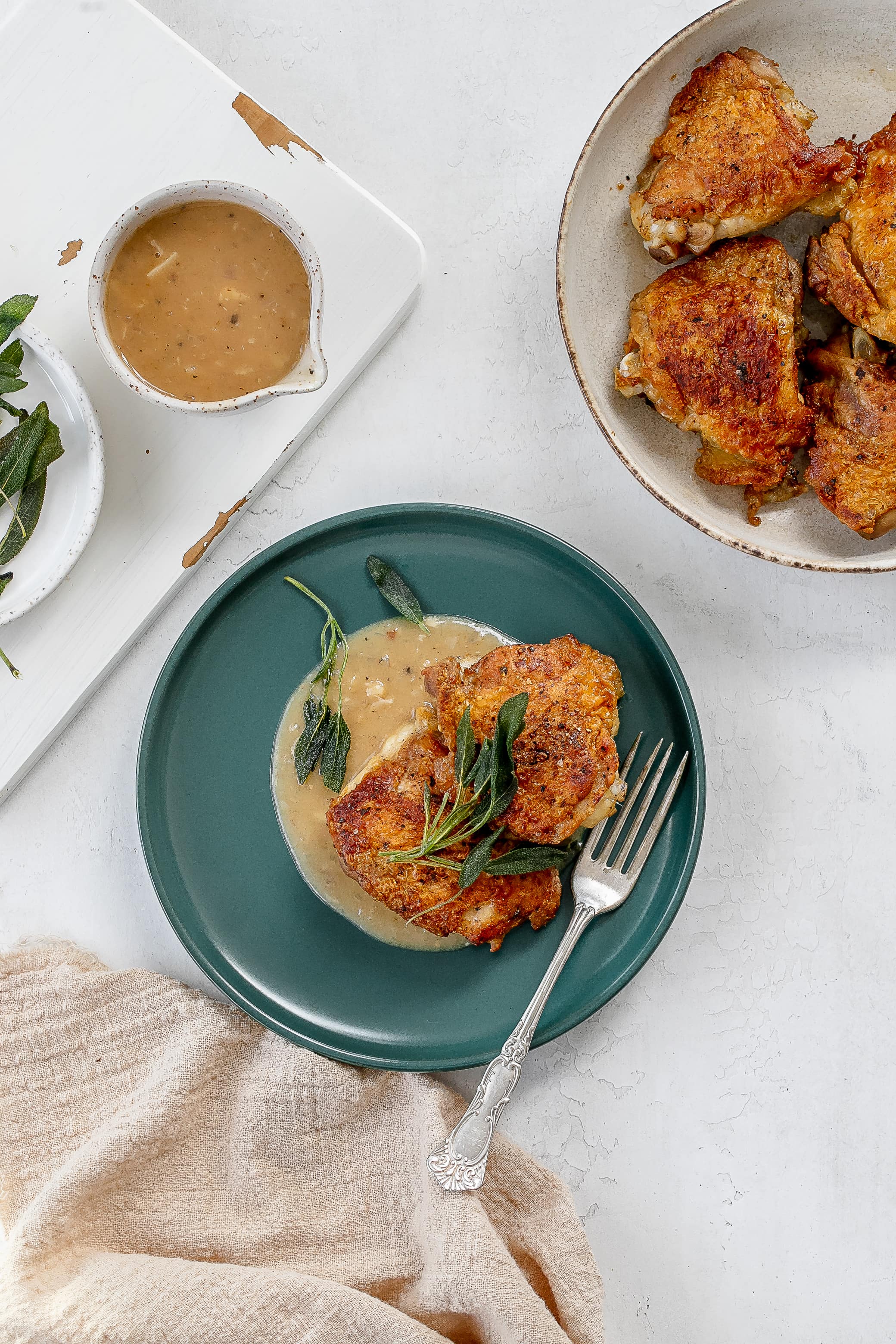 chicken thighs with sage on a plate with pan sauce.