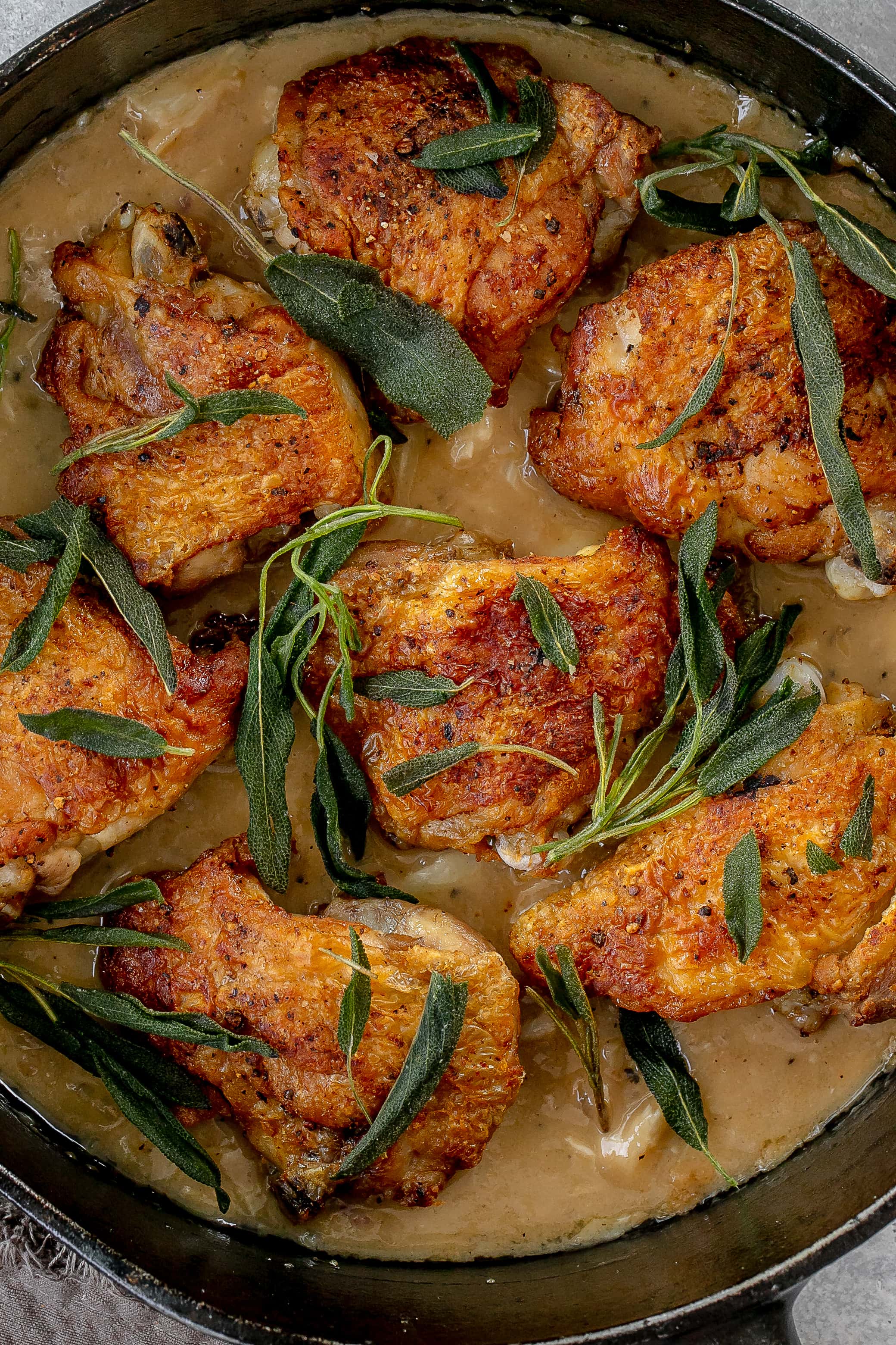 chicken thighs with sage in a skillet with pan sauce.