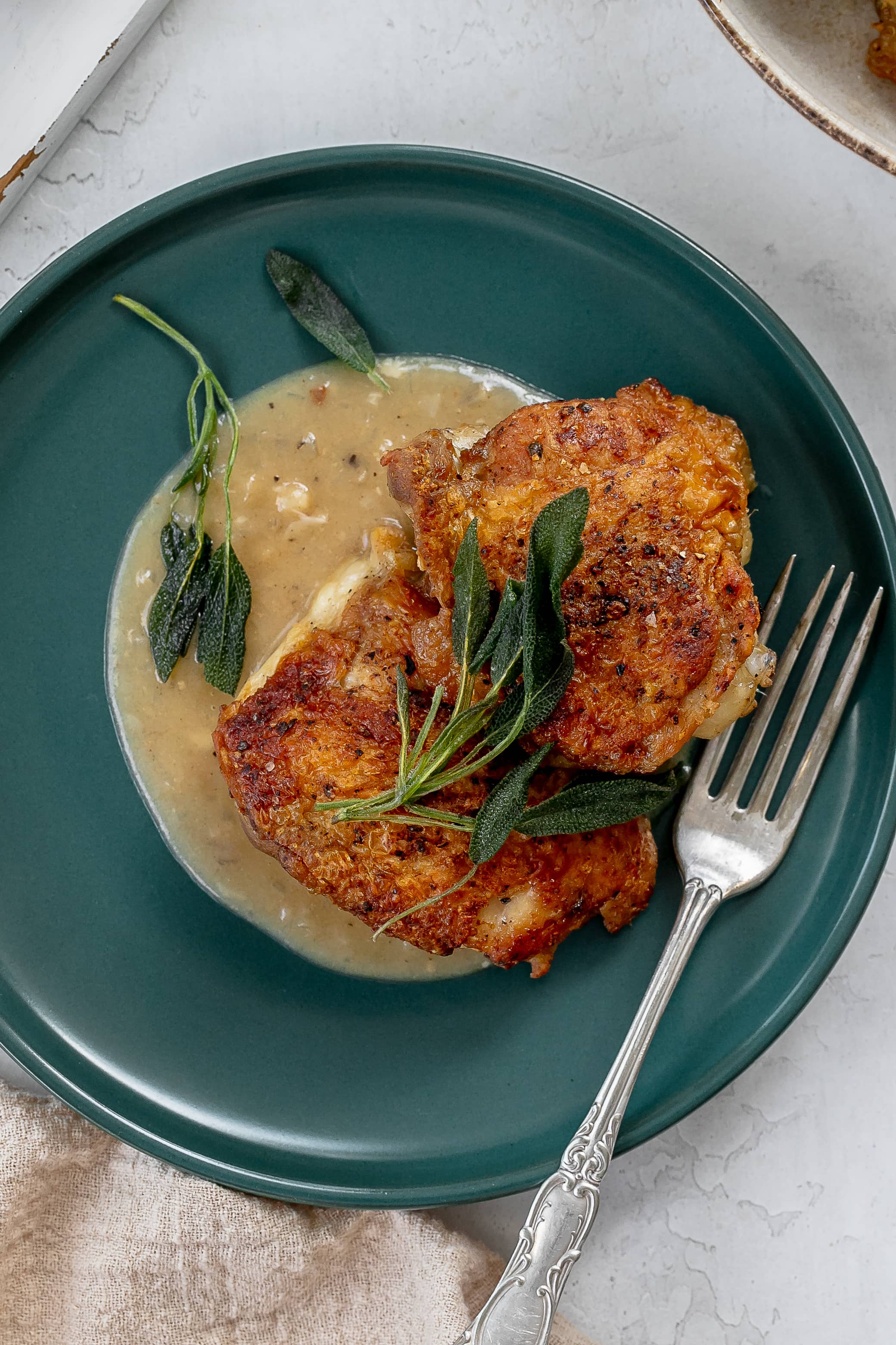 chicken thighs with sage on a plate with pan sauce.