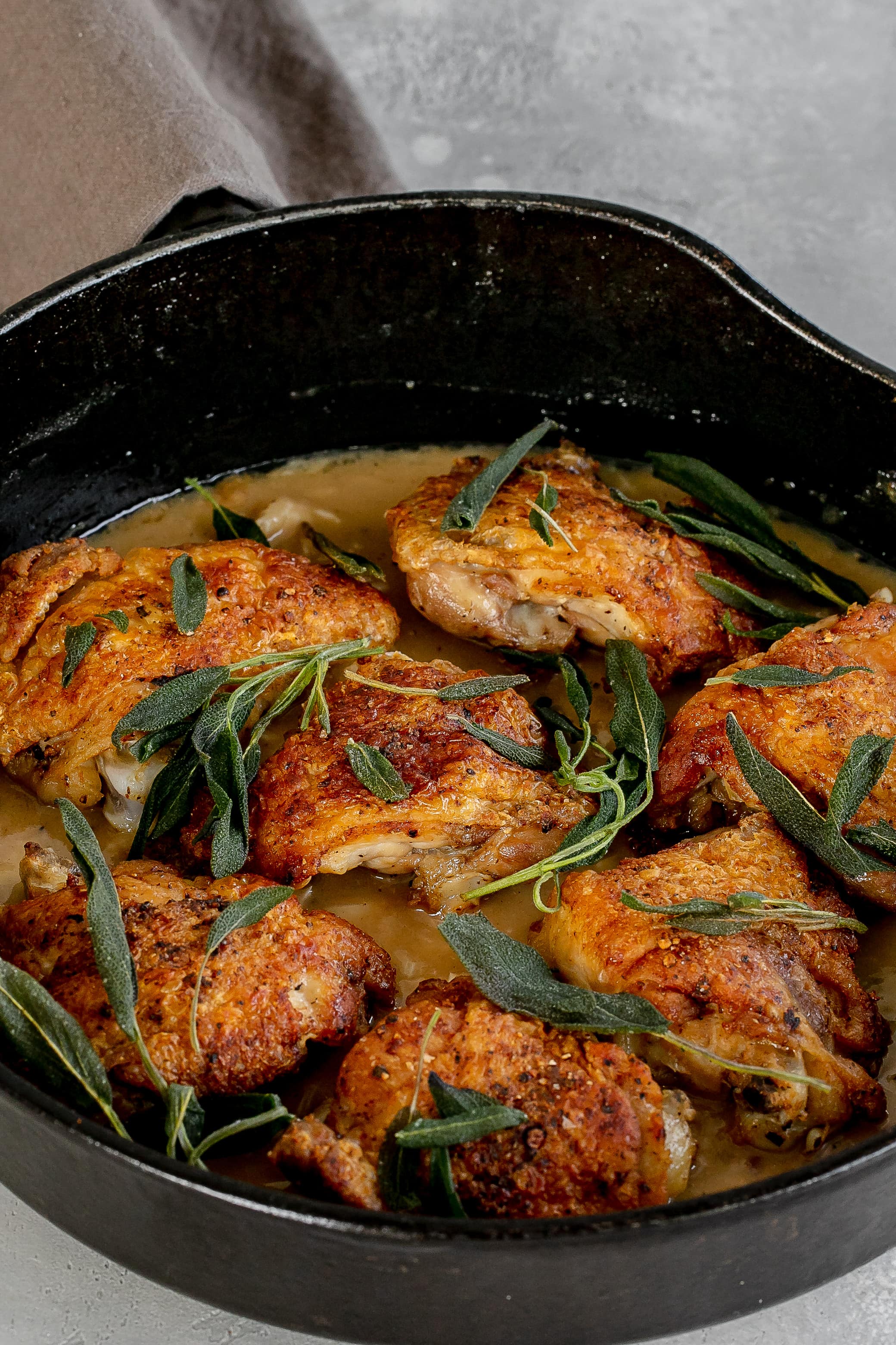 chicken thighs with sage in a skillet with pan sauce.