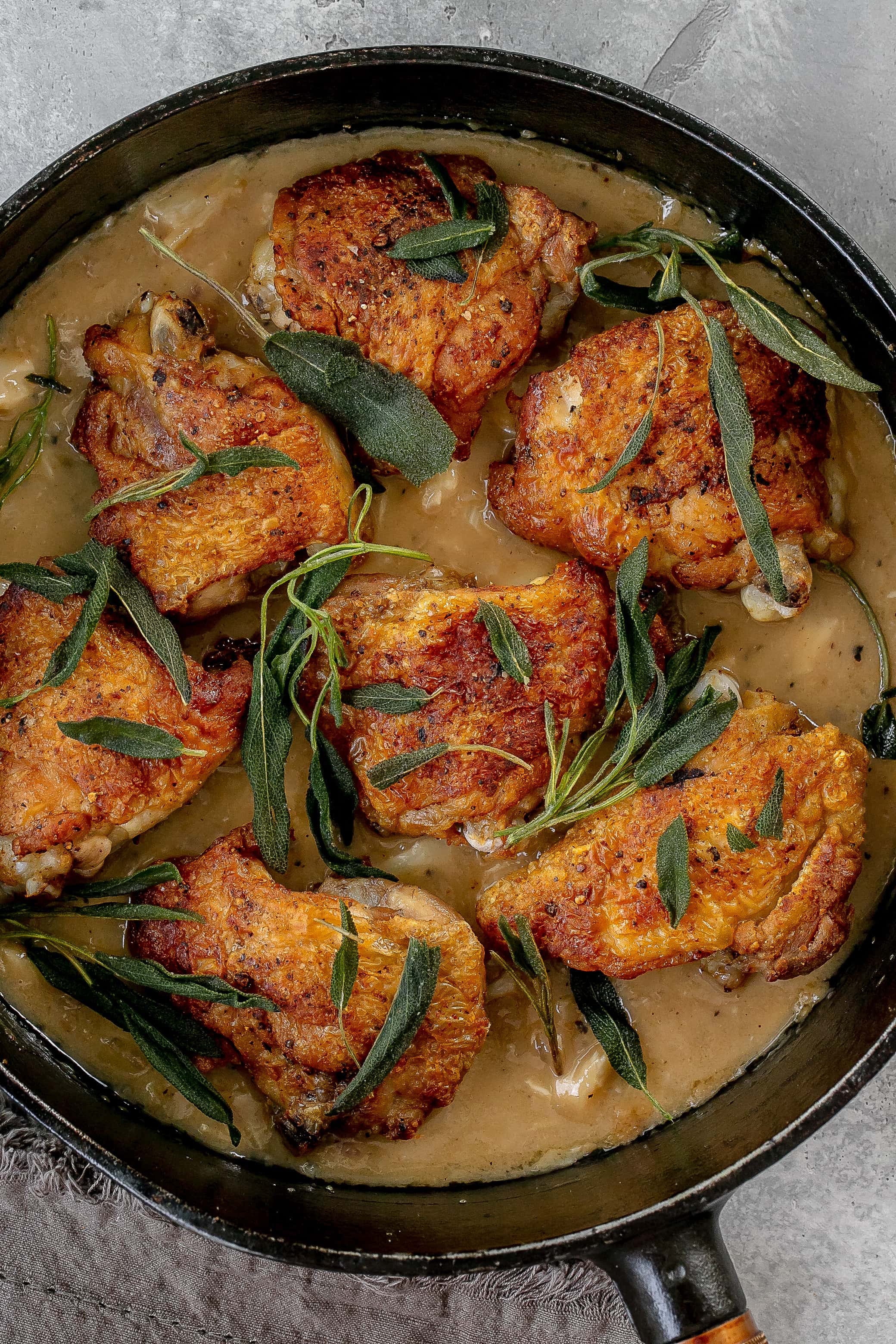 chicken thighs with sage in a skillet with pan sauce.
