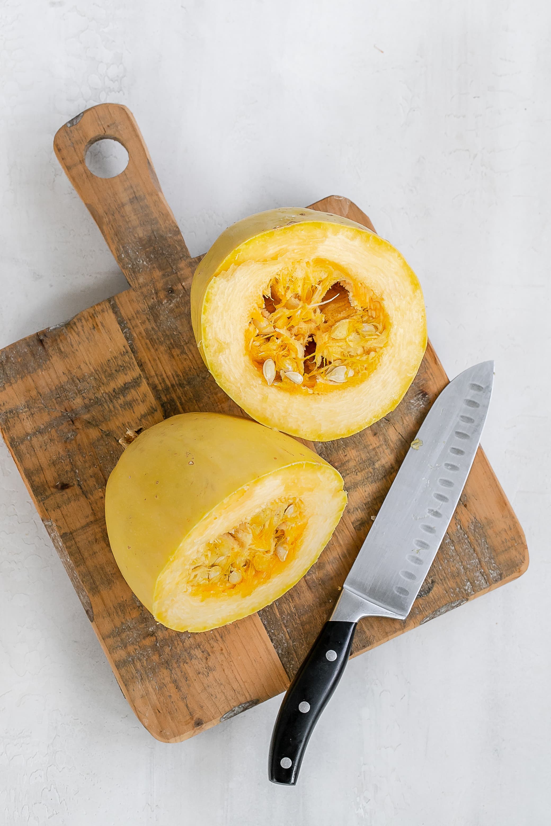 spaghetti squash cut in the middle on cutting board with knife. 