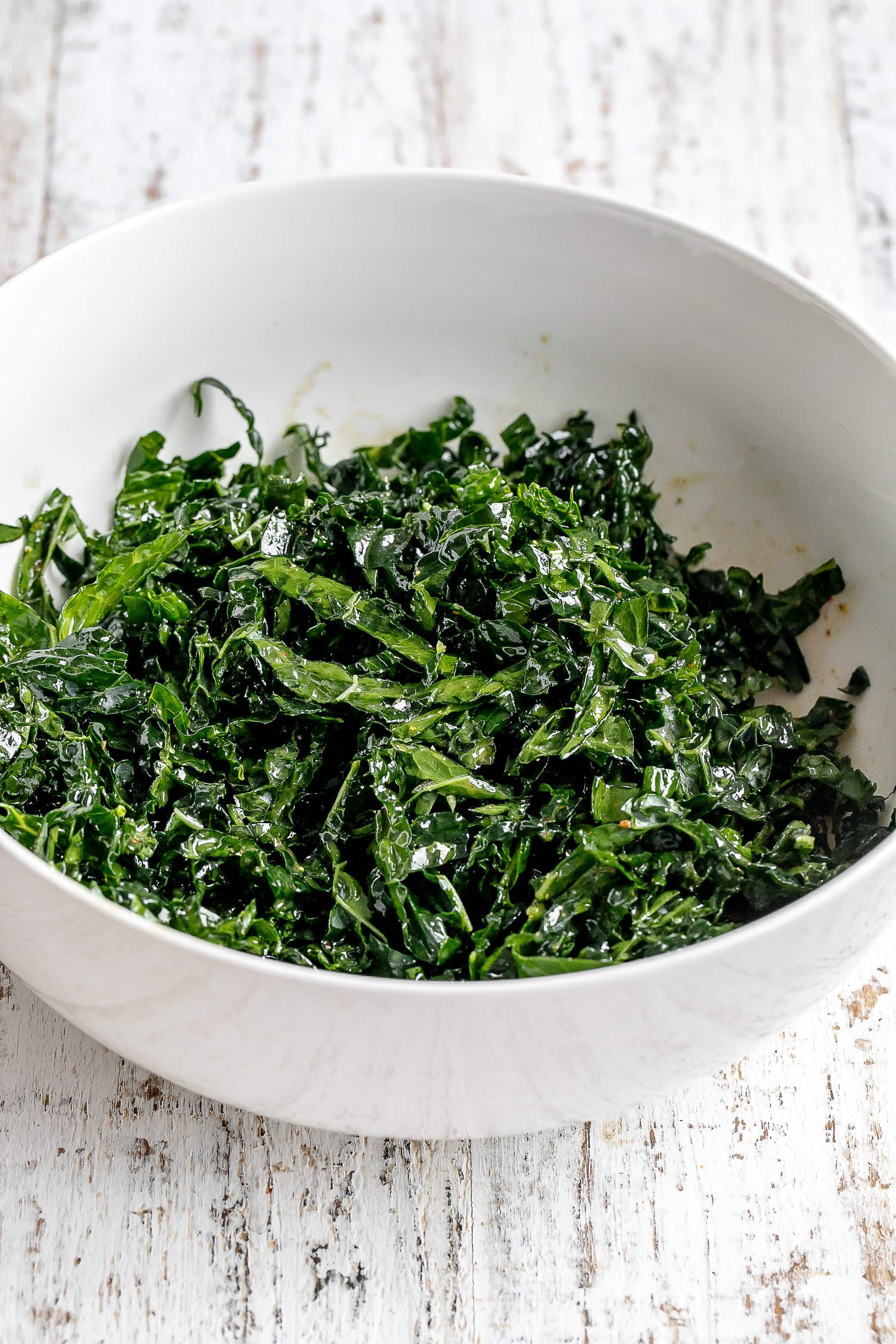 kale in a large white bowl with dressing. 