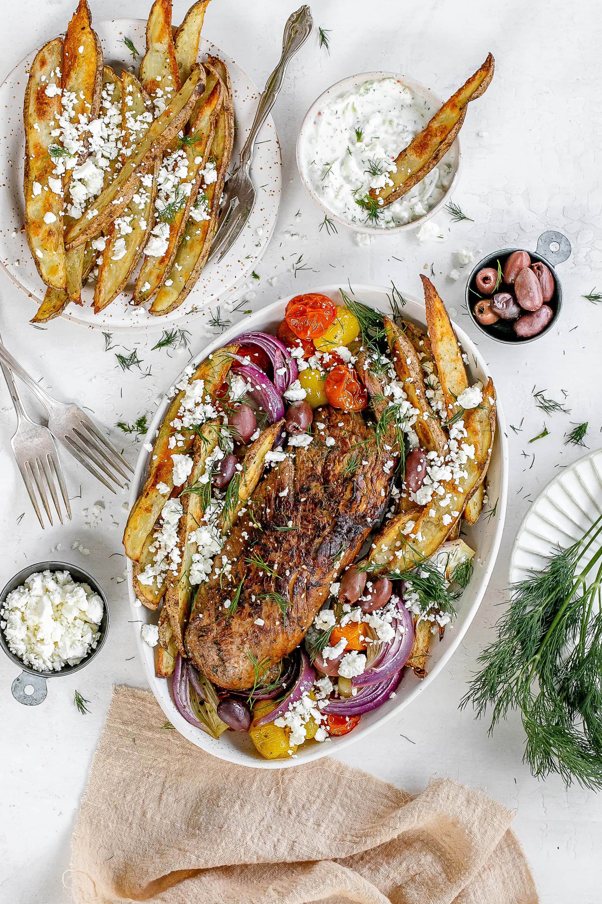 Greek pork tenderloin on serving platter with fries and veggies. 