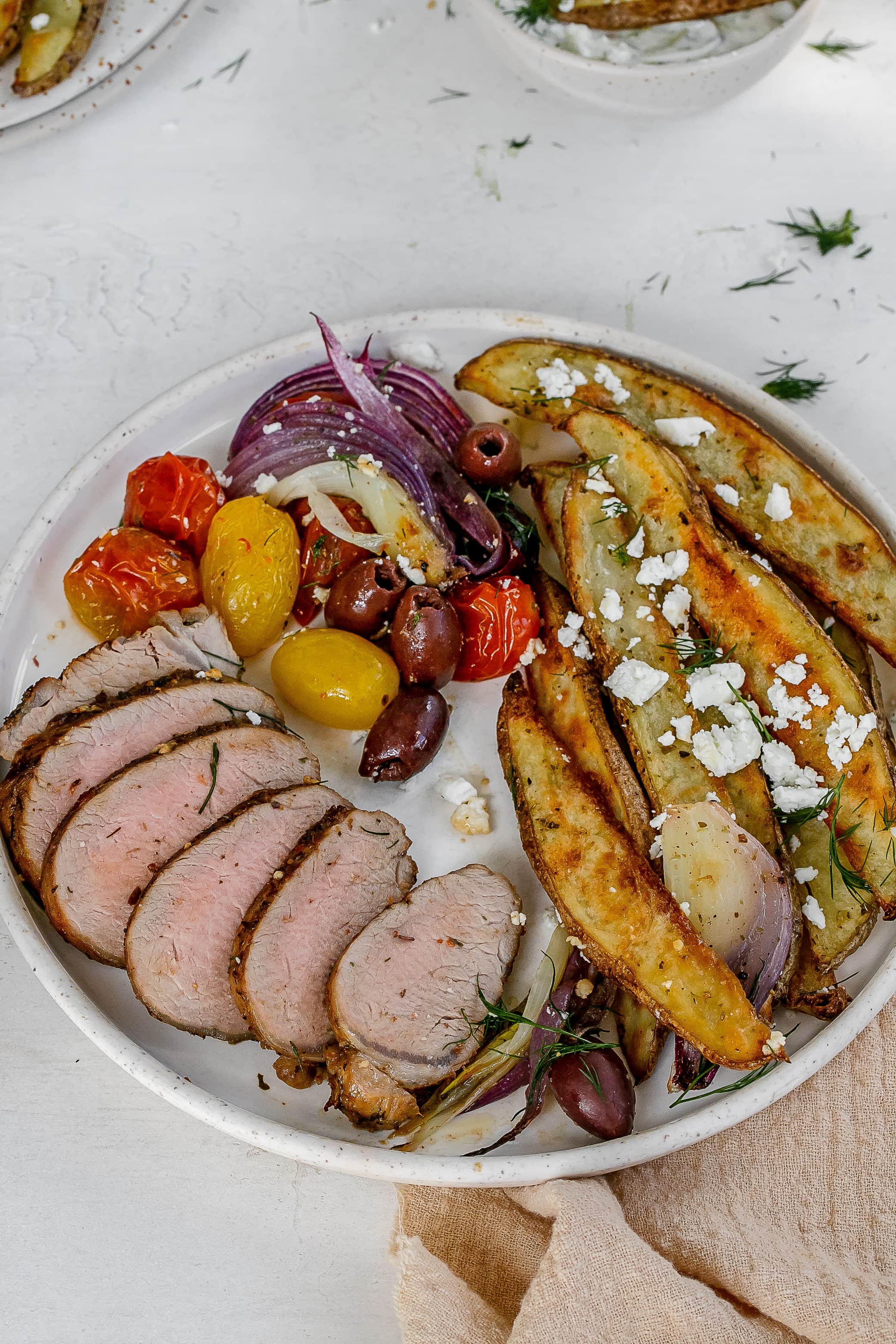 Greek pork tenderloin on a plate with fries and veggies. 