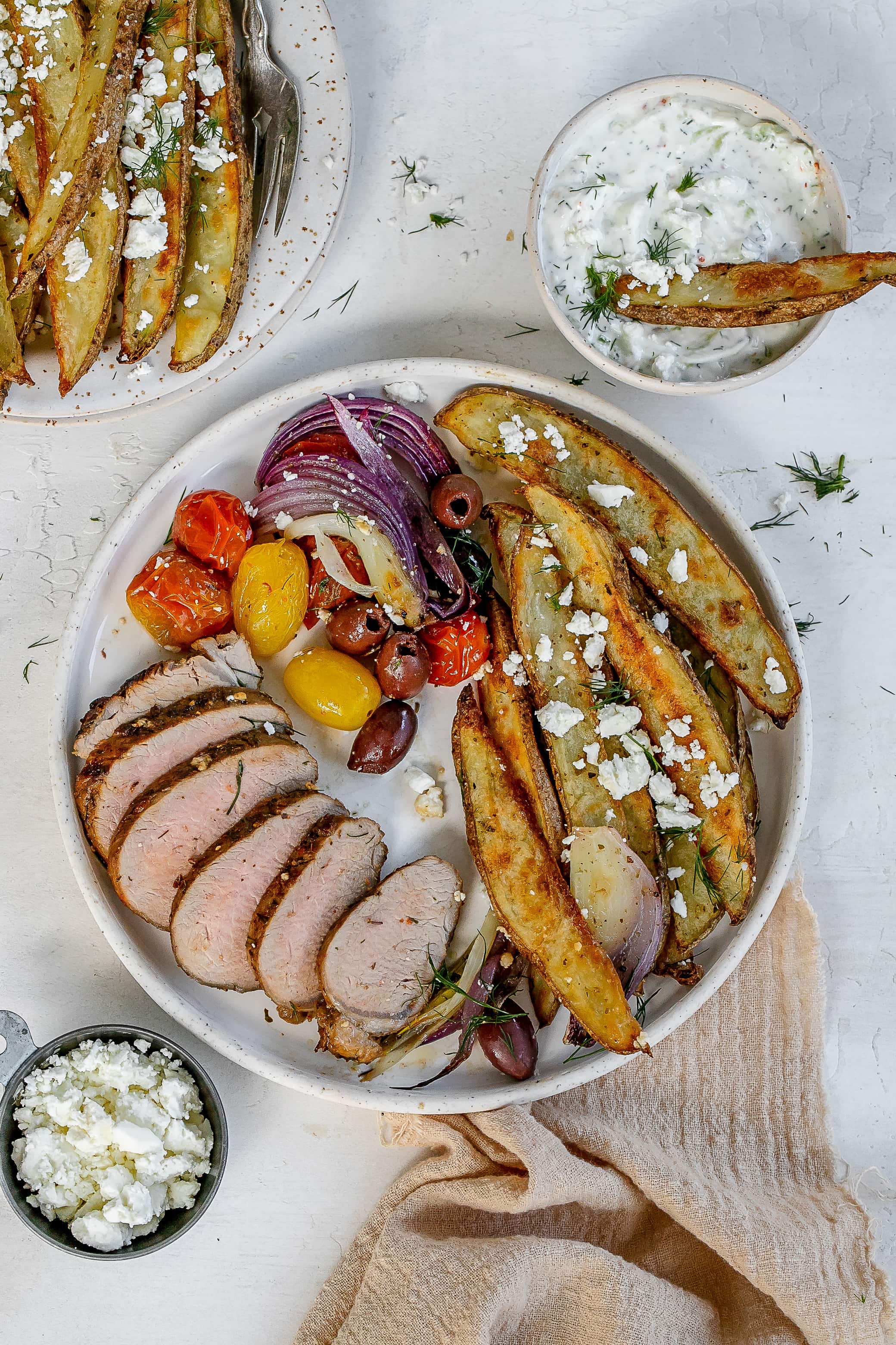Greek pork tenderloin on a plate with fries and veggies. 