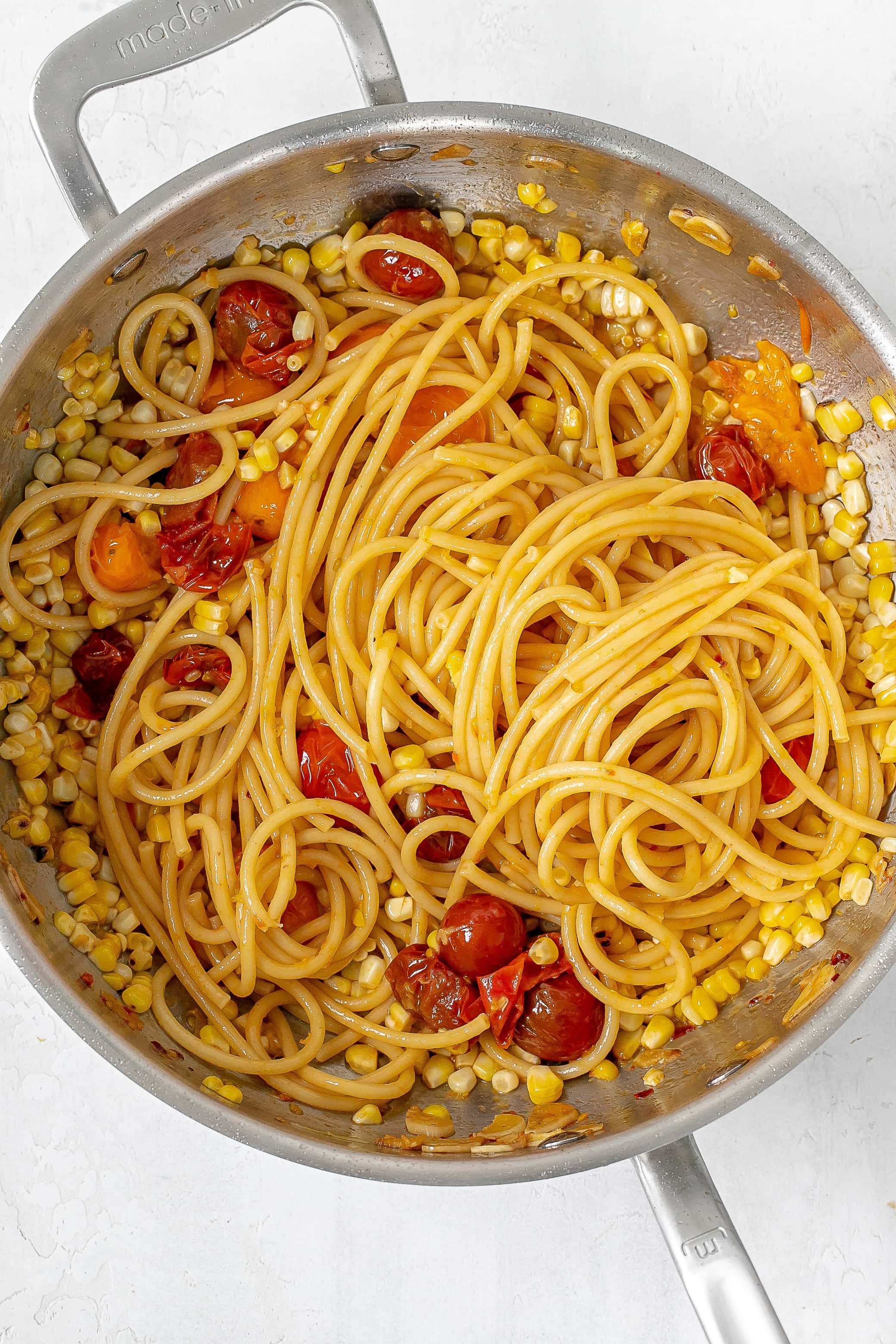 pasta added into skillet with tomatoes and corn.