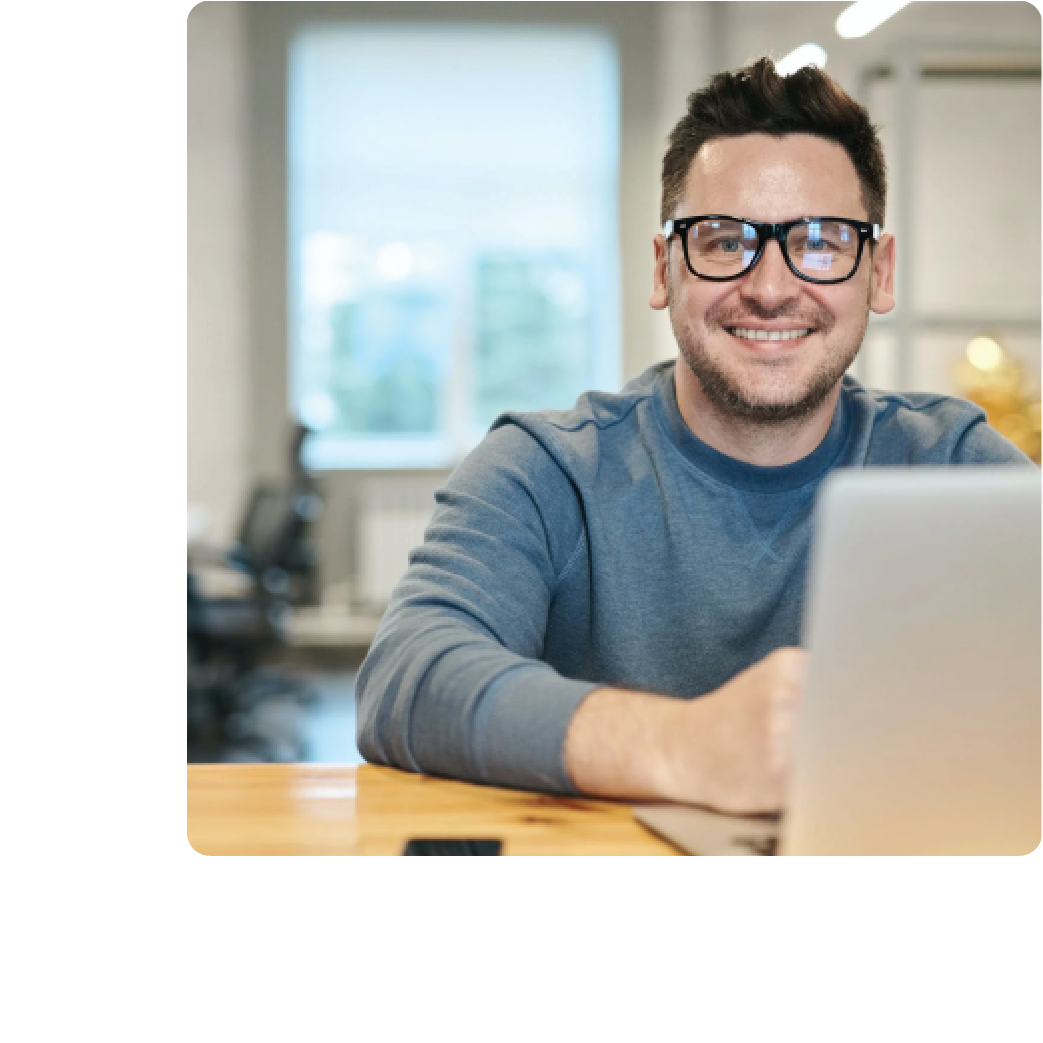 A man behind a laptop smiling at the reports he is seeing