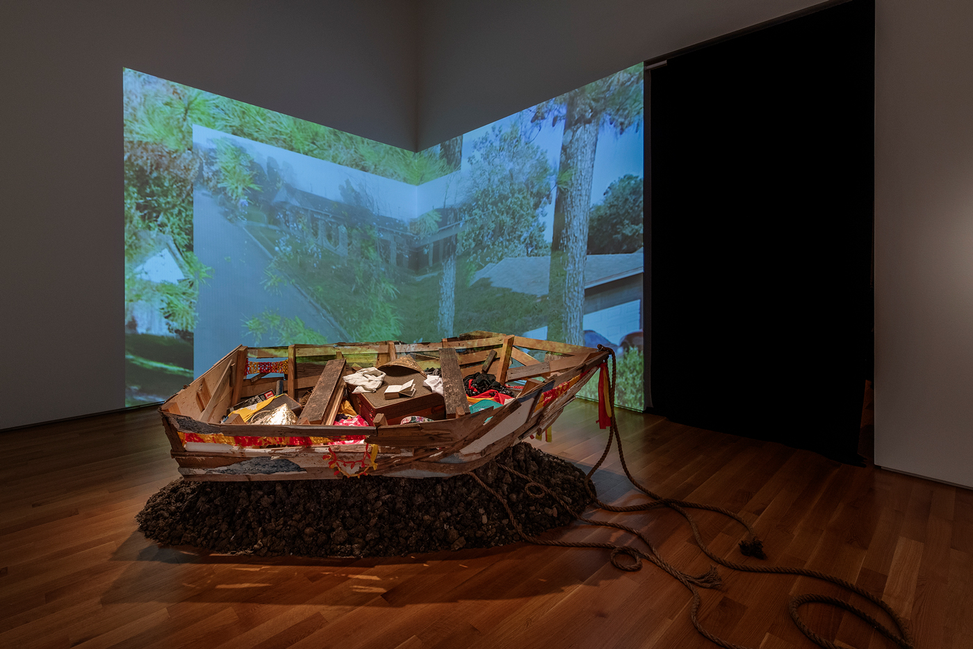 Image of an installation by Brandon Tho Harris containing a boat sculpture, and video.